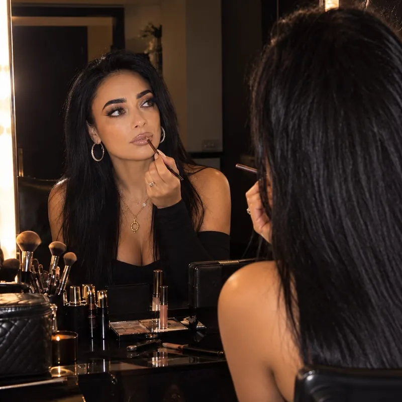 Miriam Olivia lining her lips with a lip liner in front of a mirror